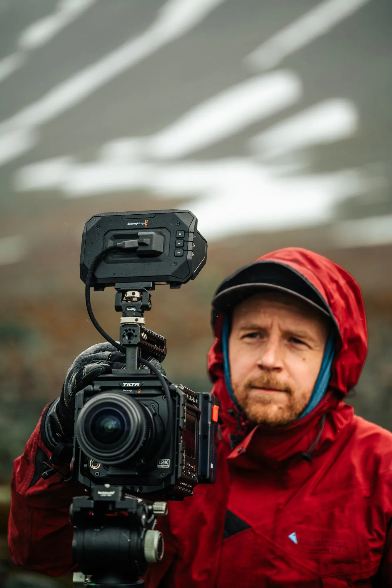 A filmmaker in a red hooded jacket holding the fulldome camera on a misty slope