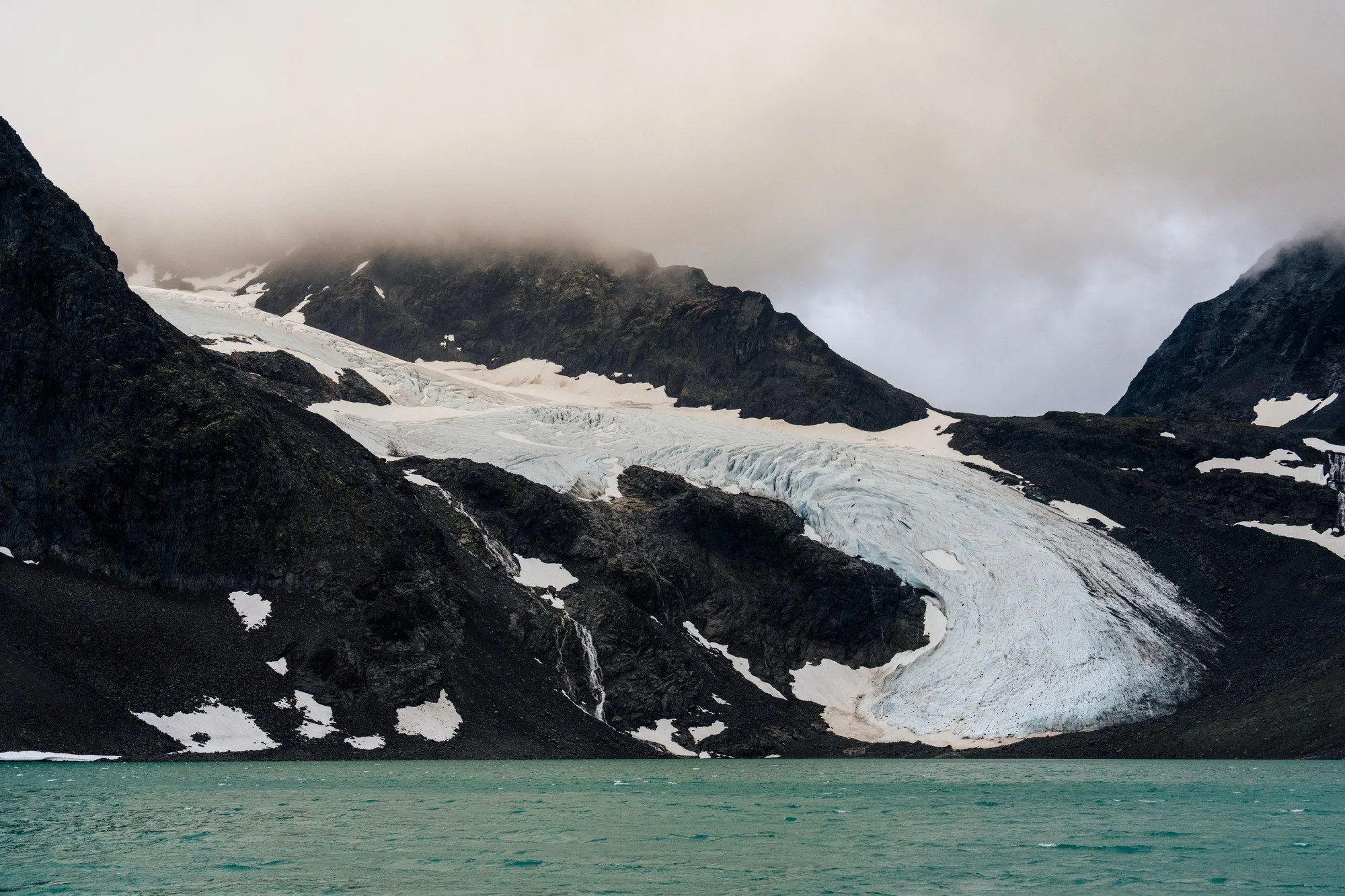 A glacier tongue descending between dark mountains to a turquoise meltwater lake
