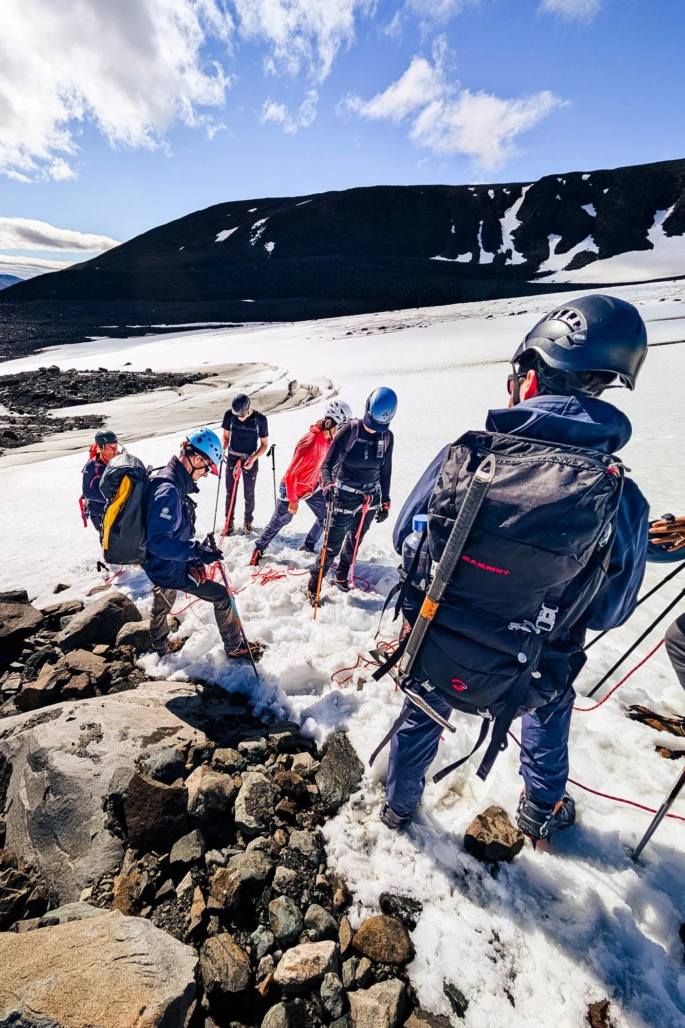 A rope team in helmets climbing down from the moraine onto the snow of the glacier