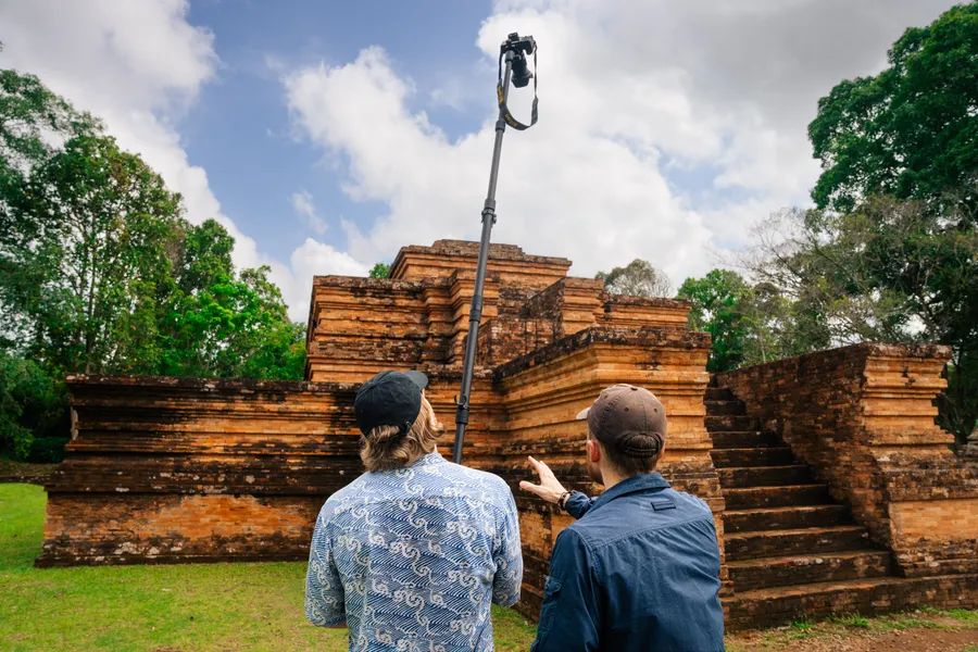A 360 camera on a pole in front of a temple, with two people checking the shot
